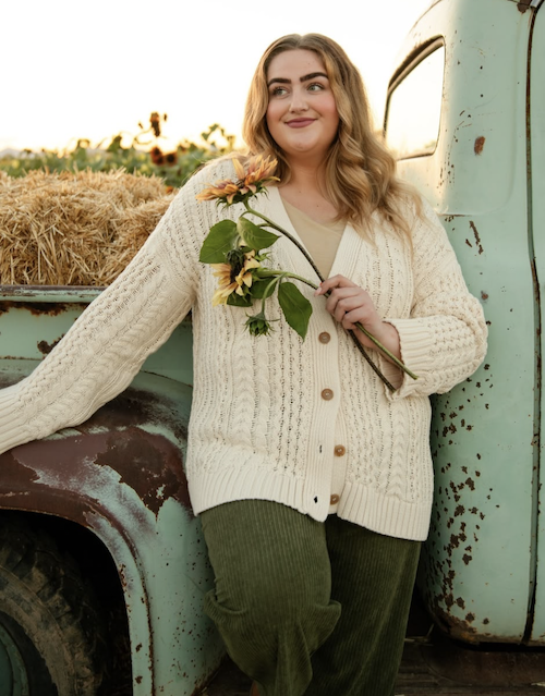 Woman wearing a cardigan and holding sunflowers in front of a truck