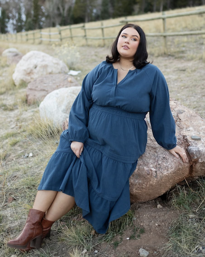 Woman sitting on a rock wearing a long blue dress and boots