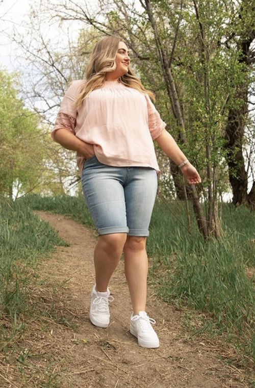 Woman walking on a dirt path in a pink tee and Bermuda shorts