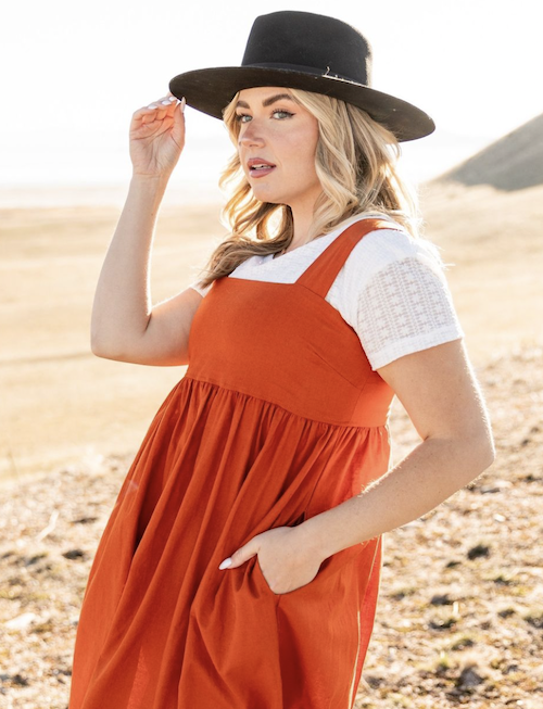 Top half of a woman wearing an orange jumpsuit and holding the tip of her