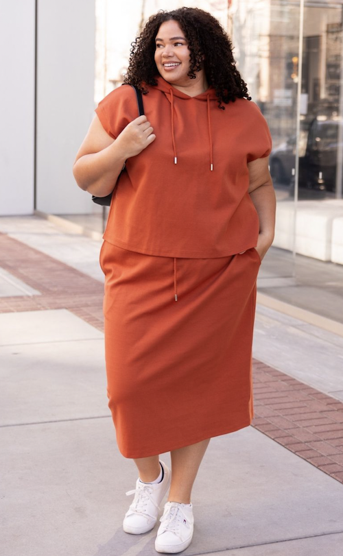 Woman outside wearing a bright orange waist tie skirt with matching top