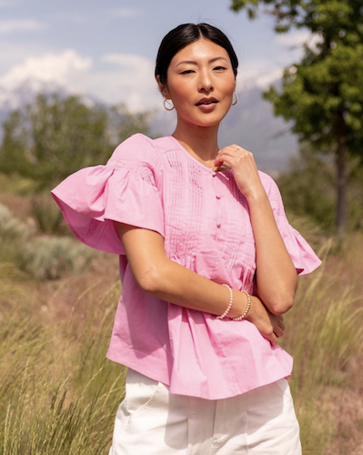 Woman standing in a field wearing a pink top with bell sleeves